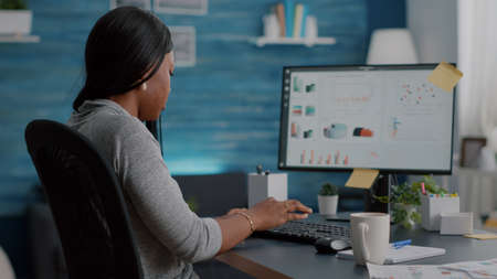 African american student analyzing financial infographics typing strategy on computer working remote...