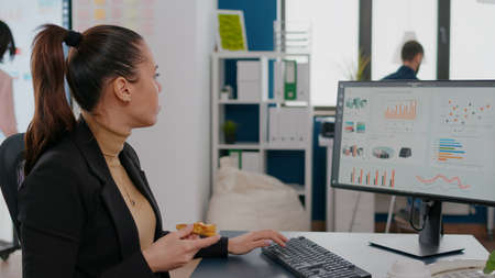 Businesswoman having delivery food order on desk during takeout lunchtime working in business company office. Entrepreneur woman eating takeaway lunch pizza slice typing management statisticsの写真素材