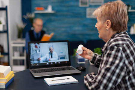 Senior woman showing pills bottle during medical online conference. Elderly woman discussing with...