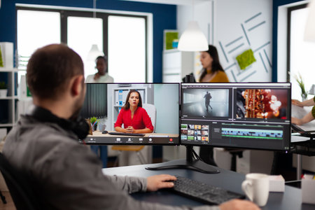Videographer in web online conference with project manager on video call editing client work, getting feedback on commercial movie using post production software on two monitors in start up officeの写真素材