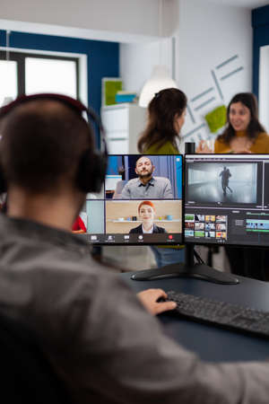 Videographer employee having video conference wearing headset editing client movie, getting feedback...