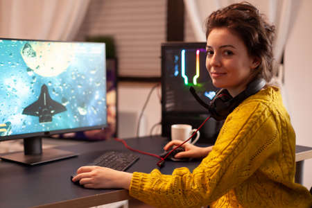 Woman gamer taking off headseat looking at camera smiling and playing in virtual shooter game...
