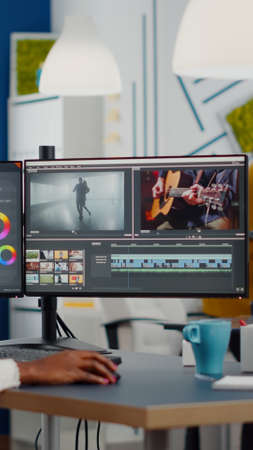 Black videographer putting on headset editing movie using post production software working in creative start up agency office. African editor processing video footage on computer with dual displaysの写真素材