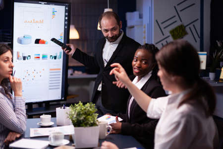 Entrepreneur man brainstorming management strategy working hard in meeting office room late at night. Diverse multi-ethnic business team looking at financial company presentation on monitor.の写真素材