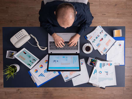 Top view of business man in corporate office sitting at desk, typing on laptop, working on financial statistics and business strategy. Entrepreneur using touchepad scrolling through documents.の写真素材