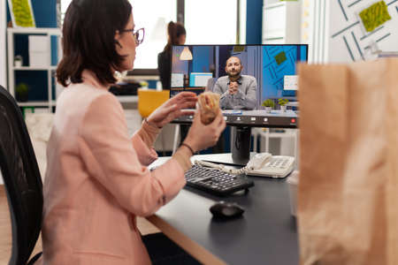 Businesswoman eating delivery takeaway sandwich during online videocall conference meeting...