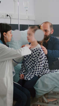 Paediatric doctor examining chest listening heartbeat using medical stethoscope while black woman nurse writing disease treatment working in hospital ward. Kid patient recovery after surgeryの写真素材