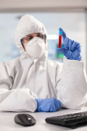 Close up of blood sample while medical researcher looking at it dressed in ppe suit. Scientist...
