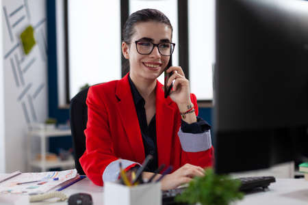 Businesswoman in office workplace privide help consulting client, distantly by mobile phone. Entrepreneur looking at document on computer screen. during phone conversation.の写真素材