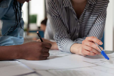 Close up of diverse architect women hands working on blueprint plans at desk. Professional engineer...