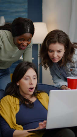 Multi-ethnic friends watching interesting comedy movie on laptop computer relaxing on couch,...
