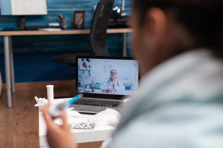 Unwell woman at home calling doctor on computer for medicine support diagnostic against illness flu cold. Caucasian patient with virus fever temperature holding thermometerの写真素材