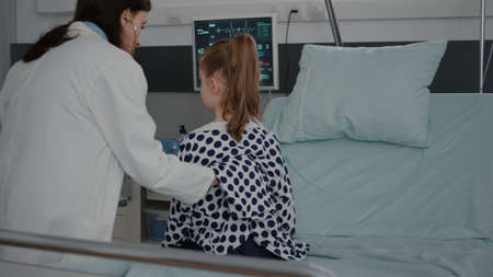 Pediatrician woman doctor examining sick patient using medical stethoscope listening heart beat during diagnosis appointment in hospital ward. Hospitalized child recovering after illness surgeryの写真素材