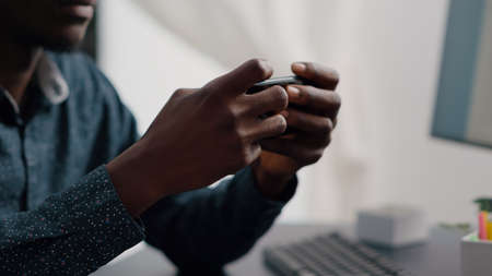 Close up of black man hands playing online internet mobile video games on his phone at home. Leisure...
