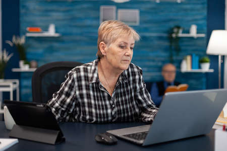 Senior business owner working from home office using portable computer. Elderly woman in home living...