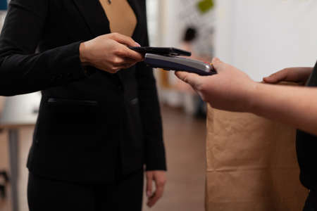 Entrepreneur doing contactless payment usint smartphone, during non cash financial transaction, for takeaway meal lunch food delivery. Client receiving fresh food in paper bag.の写真素材