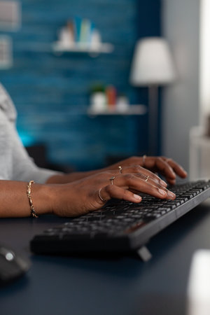 Close-up of black student hands typing on keyboard browsing online information on internet working remote at business article sitting at desk table. African american woman searching education emailの写真素材