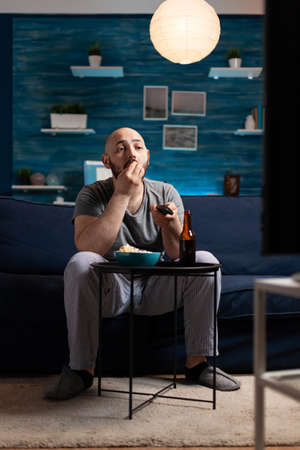 Man enjoying relax time watching tv comedy series at home sitting on comfortable couch dressed in...