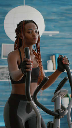 Fit athletic black woman running on elliptical bike watching wellness routine fitness video on tv...
