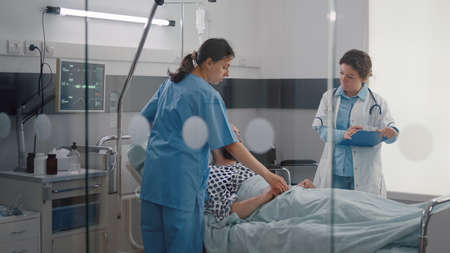 Patient sitting in bed having respiratory illness while medical nurse monitoring heart pulse in hospital ward. Sick manresting in bed while doctor analyzing pulse using medical oximeterの写真素材