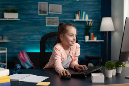 Primary schoolgirl looking at computer monitor for online class lecture on internet connection and...