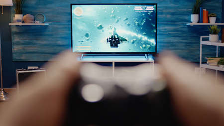 Close up of gaming TV in modern living room at home. POV of video games on television. Excited person hands playing with controller using console as entertainment activity and funの写真素材
