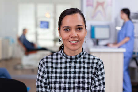 Portrait of smiling woman patient looking on camera sitting on chair in waiting room of...