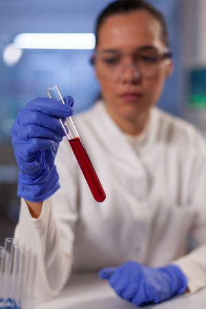 Professional chemist with test tube for blood in hand doing scientific biochemistry development in...