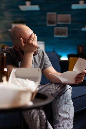 Desperate, depressed, frustrated man reading renter paper letter with banking bills crying while...