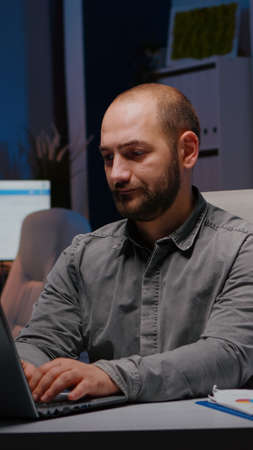 Overworked businessman typing financial statistics on laptop sitting at desk table in startup...