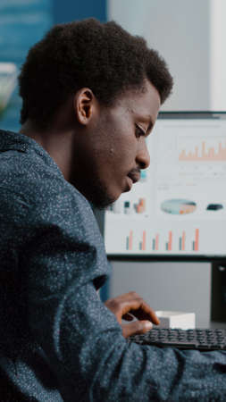 Selective focus on black american guy working from home, taking notes on notepad while remote working on computer from living room. Computer user using business internet online web communication jobの写真素材