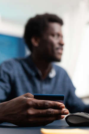Black consumer buying online with credit card typing information on app. African american man purchasing via internet payment technology and spending money for work from home projectの写真素材