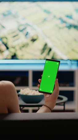 Caucasian woman holding mobile phone with green screen vertically looking at mockup template for chroma key. Young person using modern smartphone with copy space of isolated backgroundの写真素材