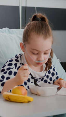 Mother sitting with sick daughter while eating healthy food meal in hospital ward during medical consultation. Hospitalized girl recovering after medical surgery having breathing sicknessの写真素材