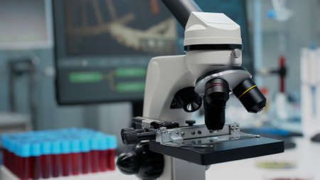 Close up of microscopic glass lens in laboratory at chemical clinic. Microbiology equipment tool used by scientists for blood or substance examination. Vacutainers and computer on deskの写真素材