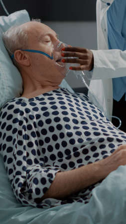 African american doctor helping sick patient in hospital ward with oxygen tube. Nurse consulting old man with stethoscope for healthcare resuscitation and illness recovery treatmentの写真素材