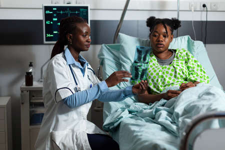 African american medic analyzing x ray scan for diagnosis on patient healthcare in hospital ward bed...