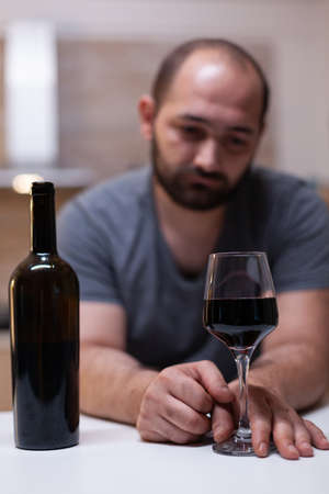 Close up of bottle and glass of wine prepared for man feeling unhappy and lonely. Person drinking alcoholic beverage, booze, liquor while being alone in kitchen. Intoxicated adultの写真素材