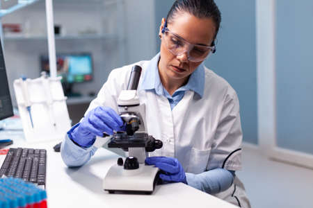 Microbiologist doctor woman analyzing vaccine results using medical microscope researching bacteriology infection diagnostics against coronavirus. Specialist doctor working in biotechnology laboratoryの写真素材