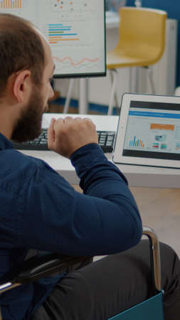 Disabled handicapped immobilized paralyzed manager man using computer and tablet in same time...