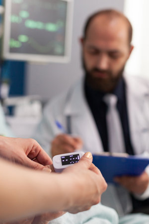 Asisstant nurse puts medical oximeter on finger while doctor man writes heartbeat puls rate on clipbord during consultation. Social services nursing elderly retired female. Healthcare assistanceの写真素材