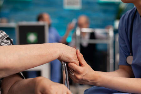 Assistant support worker holding disabled senior female patient hands consoling during therapy....