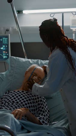 African american doctor placing oxygen tube on patient in hospital ward at medical reanimation...