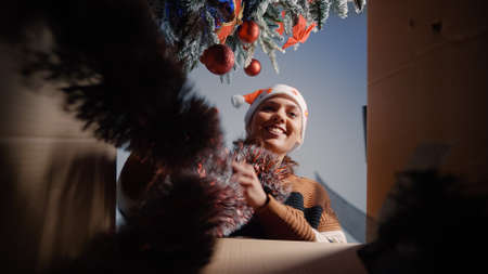 Woman opening box of christmas ornaments for winter season decorating at home. Young caucasian adult getting excited about garlands and globes for green tree preparing for festivityの写真素材