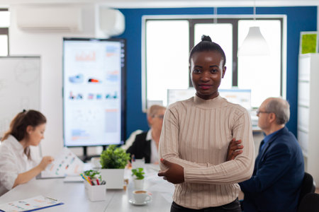 Successful smiling african business woman holding arms crossed looking atcamera in conference room. Manager working in professional start up financial business, modern company workplace ready for meeting.の写真素材
