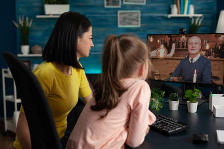 Little kid and mother doing virtual meeting with relatives on online internet website. Family using digital video call modern technology to talk to grandpa at home social distancingの写真素材