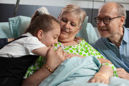 Family visiting sick retired senior woman in hospital ward during clinical therapy. Caring...