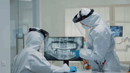 Professional stomatologist looking at teeth animation on screen and comparing model for patient dentition at clinic. Dental assistant using virtual computer technology for operationの写真素材