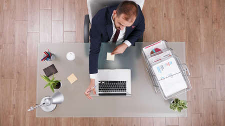Top view of businessman putting stickey notes on laptop while working at company investments planning management strategy in startup office. Project leader brainstorming business ideasの写真素材