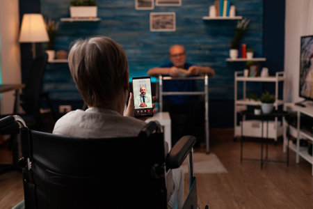 Woman in wheelchair calling doctor using video call technology on smartphone sitting at home asking...